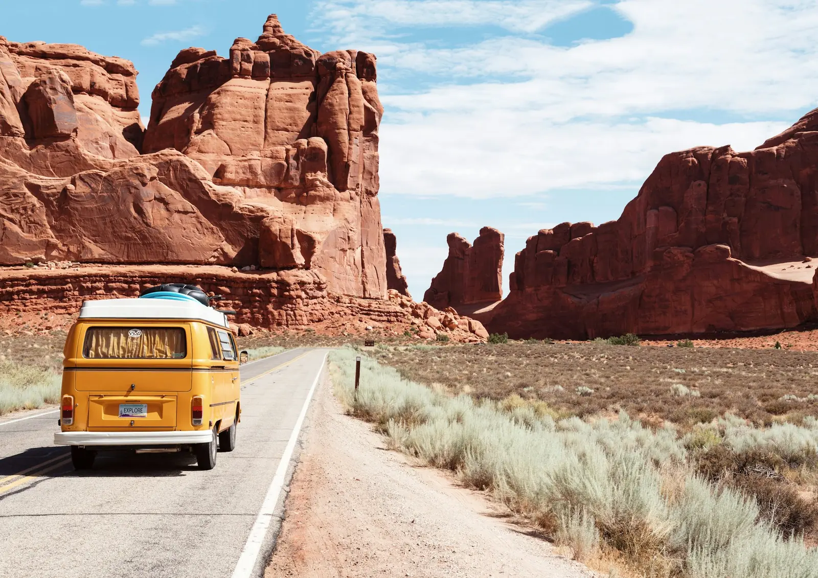 Gele camperbus op een woestijnweg tussen rode rotsen in Utah