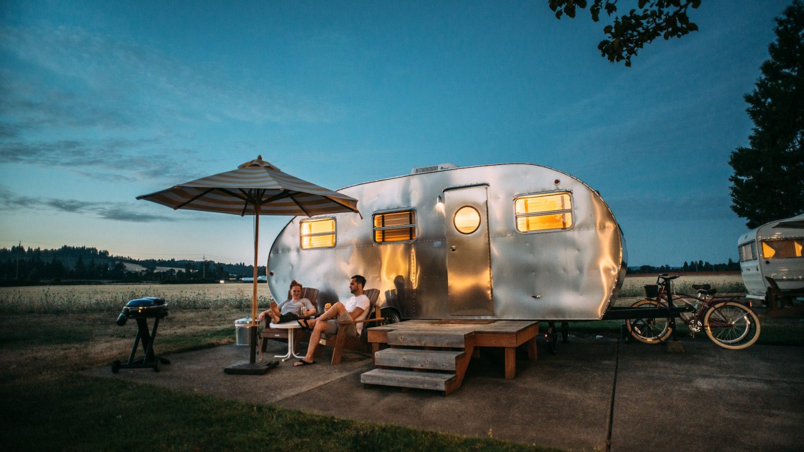 Zilveren caravan met luifel en terras op een camping bij avondlicht