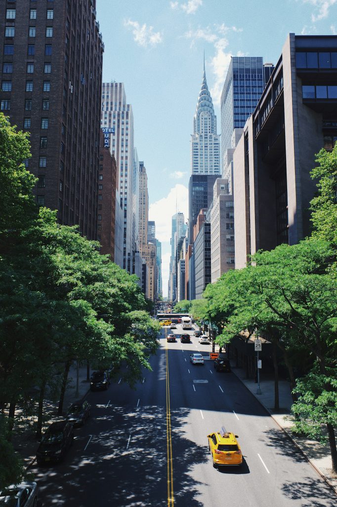 Zonnige straat in Manhattan met een gele taxi en groene bomen